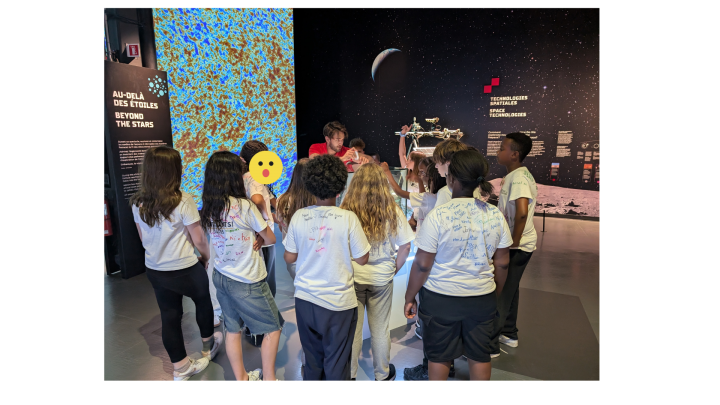 Groupe d'élèves avec un animateur devant un tableau représentant des étoiles.